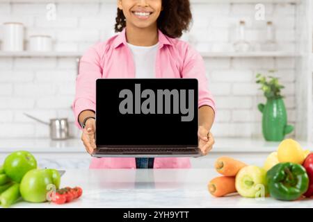 Irriconoscibile ragazza nera che tiene il laptop in cucina Foto Stock