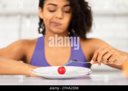 Afro donna che guarda il pomodoro piccolo su un piatto Foto Stock