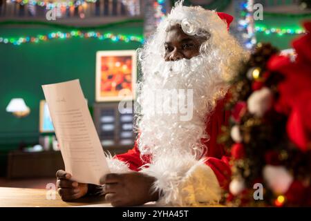 Babbo Natale legge lettere di Natale nella sua accogliente cabina al Polo Nord, circondato da decorazioni festose e luci scintillanti. Tradizione e magia danno vita al festeggiamento natalizio con regali. Foto Stock