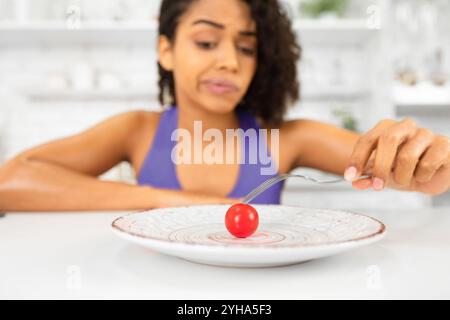 Infelice afro donna che guarda il pomodoro piccolo su un piatto Foto Stock