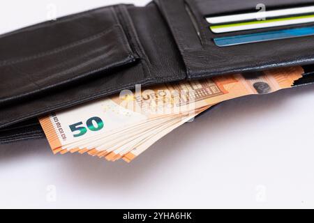 Portafoglio uomo aperto in pelle nera con cinquanta banconote da euro e carte bancarie all'interno su sfondo bianco. Una borsa piena di denaro e carte di credito che simboleggia ricchezza, successo e status sociale Foto Stock