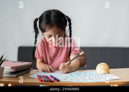 Bambino curioso impegnato in attività didattiche con materiali e libri colorati a casa Foto Stock