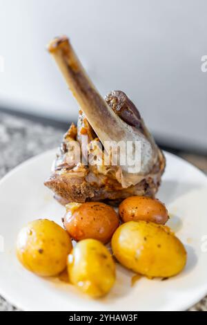 Stinco di agnello arrosto carne bruna cotta macro con patate su piatto bianco Foto Stock