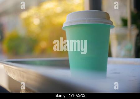 Una tazza da caffè usa e getta verde menta elegante e alla moda si trova su un tavolo all'aperto in un ambiente elegante Foto Stock