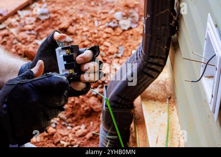 Cavi elettrici tenuti da un elettricista durante il fissaggio di una presa all'esterno della parete Foto Stock