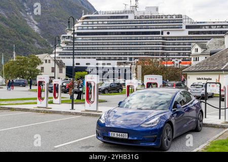 Tesla Model 3 presso un sovralimentatore pubblico Tesla nel villaggio norvegese di Eidfjord, con MS Rotterdam della linea Holland America sullo sfondo Foto Stock