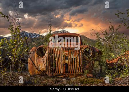 Vecchio camion d'epoca arrugginito, annidato nella natura selvaggia con sfondo montano estivo. Imbocca North Canol Road nel territorio dello Yukon, Canada Foto Stock