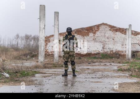 Un soldato delle forze speciali con un fucile automatico che indossa una maschera per casco e un'armatura per il corpo si erge sullo sfondo di edifici distrutti. L'abisso Foto Stock