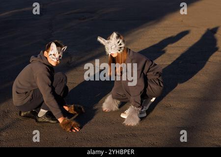 Ragazza e ragazzo quadrober in maschera gatto siedono in città, bambini quadroberi, sottocultura Foto Stock