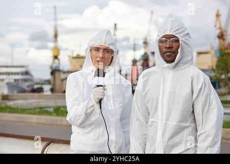 Ritratto in vita di due giornalisti che indossano tute protettive che lavorano sul posto e discutono di questioni industriali, copia dello spazio Foto Stock