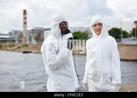 Ritratto in vita di due giornalisti che indossano tute di nocciola che parlano al microfono lavorando sul sito industriale e discutono di ecologia, spazio di copia Foto Stock