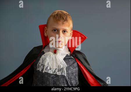 Ritratto di un ragazzo che indossa un costume da vampiro con un mantello rosso e nero e un jabot bianco in pizzo. Foto Stock