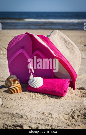 Cappello di paglia, pantofole rosa e soffice asciugamano sulla sabbia in spiaggia. Accessori per il relax in estate Foto Stock