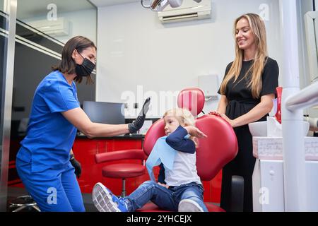 dentista che mette la mano in modo che il bambino seduto sulla sedia del dentista ottenga un cinque alto dopo il trattamento. Foto Stock