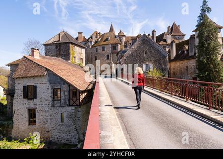 Giovane donna bionda che cammina sul ponte con l'antica città di Carennac sullo sfondo Foto Stock