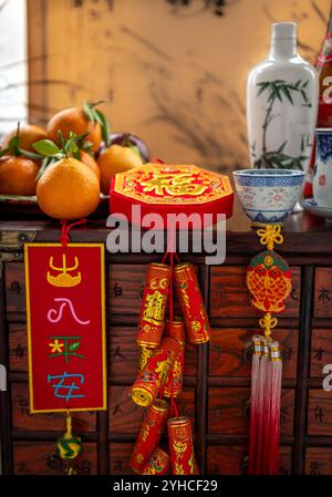 Buona fortuna e benessere, decorazioni per il Capodanno cinese, una bottiglia di vino con tazze e un piatto di mandarini e mele rosse. Un backg di Capodanno lunare Foto Stock