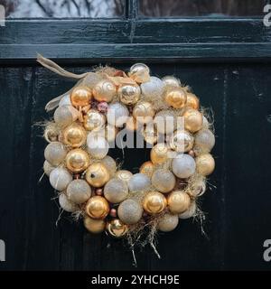 Una corona decorativa in oro e argento con scintillio e nastri appesi su una porta verde scuro nei Paesi Bassi. Foto Stock