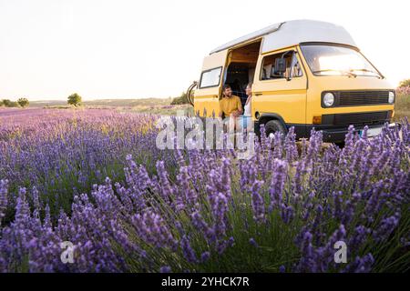 Giovane coppia felice che si gode la vista sul loro camper giallo retro all'alba nei campi di lavanda di Valensole in Provenza, Francia Foto Stock