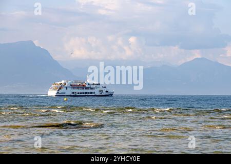 Sirmione, Italia - 21 settembre 2024: Un traghetto attraversa le calme acque del Lago di Garda con le montagne che offrono uno sfondo tranquillo Foto Stock