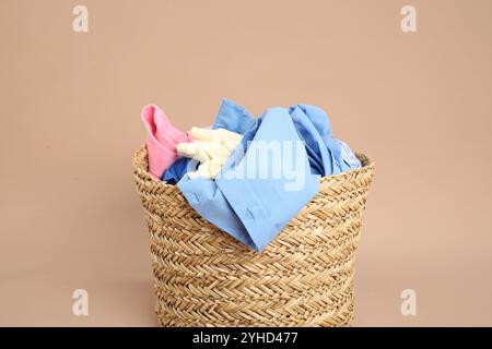 Cestino in vimini pieno di bucato su sfondo beige Foto Stock