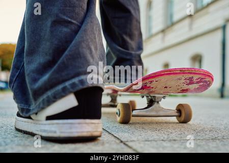 Skateboarder su skateboard rosa. Primo piano di piedi adolescenti con jeans e sneakers nere skateboard alle scale della strada. Attività ricreative AN Foto Stock