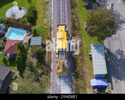 Il treno giallo passa su rotaie attraverso un villaggio, circondato da case e giardini, macchina per la compattazione, Hermann Hessebahn, Althengstett, Foresta Nera, tedesco Foto Stock