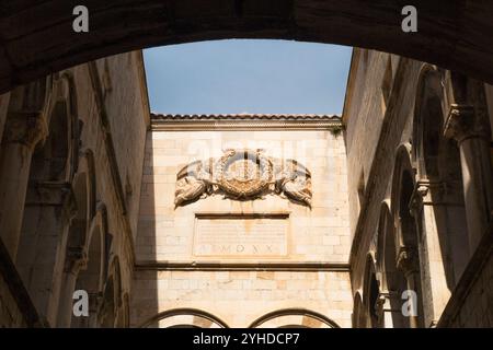 Scultura in pietra, con le iniziali di Cristo circondate da allori e angeli, dello scultore rinascimentale francese Bertrandus / Beltrand Gallicus. Situato in alto nel cortile interno dell'atrio del Palazzo Sponza (croato: palača Sponza) chiamato anche Palazzo Divona. Dubrovnik, Croazia. (138) Foto Stock