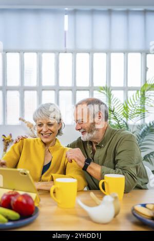 Foto verticale di una coppia matura e felice del caucaso con un tablet digitale che si diverte a casa Foto Stock