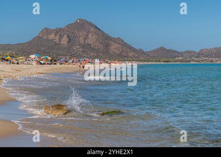 Un'onda si schianta su una roccia sulla spiaggia sabbiosa di piscina Rei, Sardegna, Italia Foto Stock