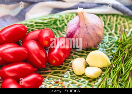 Pomodori prugna, aglio e rosmarino sul piatto verde. Primo piano Foto Stock