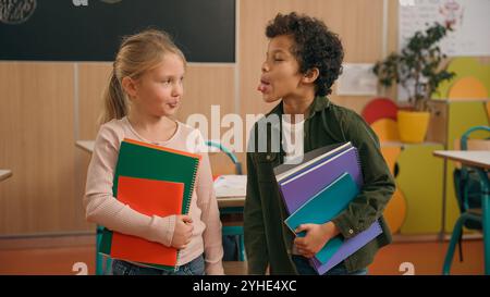 Due allievi allegri e cattivi bambini diversi ragazzi multietnici ragazzo afroamericano e ragazze caucasiche compagni di classe che si divertono a spingere ciascuno Foto Stock