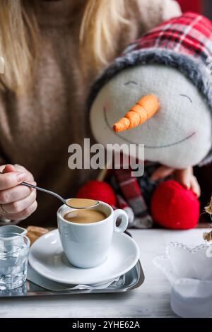 Donna che beve un caffè in un bar e tiene in mano decorazioni natalizie. Foto Stock