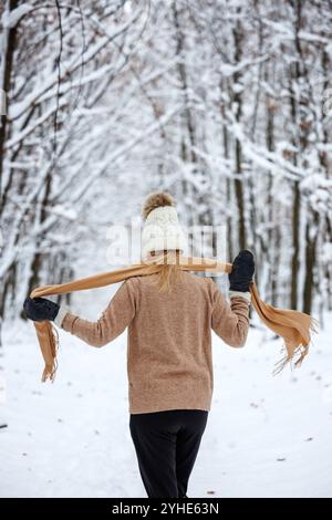 Donna che indossa un maglione, un cappello da bobble lavorato a maglia e una sciarpa nella foresta di neve. Donna che ama passeggiare nella natura invernale Foto Stock