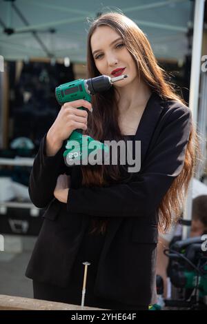 Una giovane donna elegante che regge con sicurezza un trapano elettrico in un ambiente moderno e contemporaneo Foto Stock
