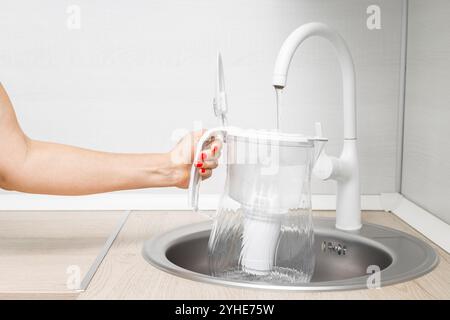 la casalinga versa acqua nel filtro dell'acqua in cucina. donna che riempie il filtro dell'acqua nel lavandino della cucina. filtro dell'acqua a forma di caraffa. Foto Stock