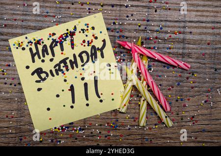 Nota adesiva gialla con buon compleanno e spolverette di caramelle e candele Foto Stock