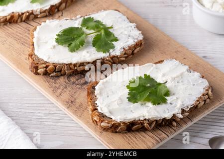 Fette preparate al momento di abbondante pane multigrano ricoperte da cremosa spalmazione e foglie di coriandolo su un asse di legno Foto Stock