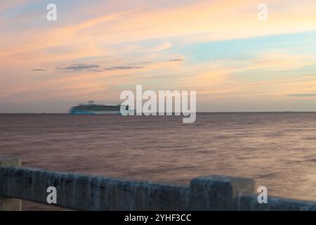 Un tramonto sereno proietta calde sfumature sulla Baia di Tampa, creando un'atmosfera tranquilla. Un movimento sfocato in lontananza da una nave che passa, aggiungendo un elemento dinamico Foto Stock