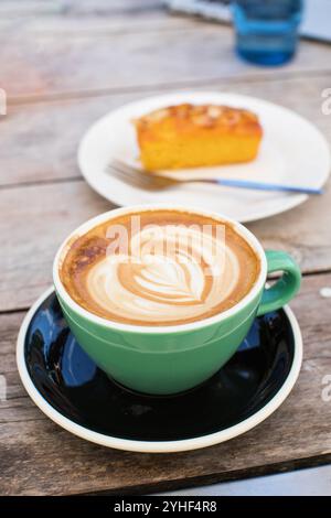 Caffè fresco decorato con cuore crema e torta sul tavolo Foto Stock