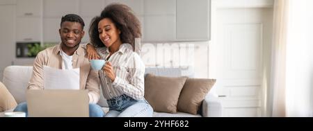 Coppia felice che si gusta un caffè insieme mentre lavora su un notebook a casa Foto Stock