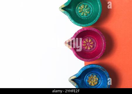 Tre vivaci lampade a olio Diwali tradizionali su sfondo arancione e bianco, perfette per design festivi, auguri di Natale e cultura Foto Stock