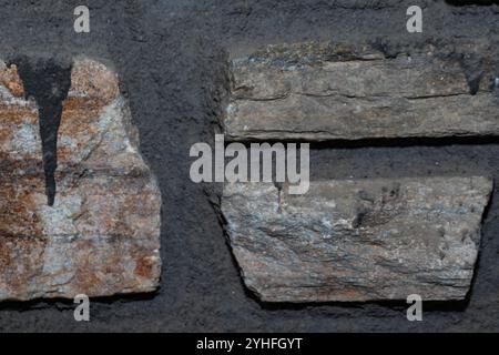 Vista dettagliata di un muro rustico in pietra con varie dimensioni e colori di pietra, adagiato su uno sfondo di Malta scura e grossolana Foto Stock