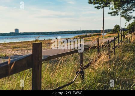 Un sentiero costiero delimitato da una recinzione di legno corre lungo una costa erbosa, offrendo una vista tranquilla e panoramica dell'oceano sotto un cielo blu brillante Foto Stock