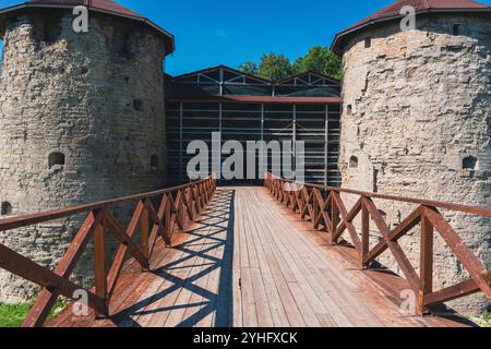 Un grande ingresso ad un'antica fortezza, caratterizzata da torri gemelle in pietra con tetti rossi collegati da un ponte di legno sotto un cielo azzurro. Un mediev iconico Foto Stock