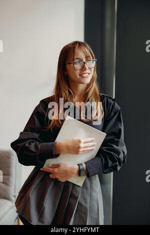 Una donna sicura di sé vestita da professionista ha in mano un notebook Foto Stock