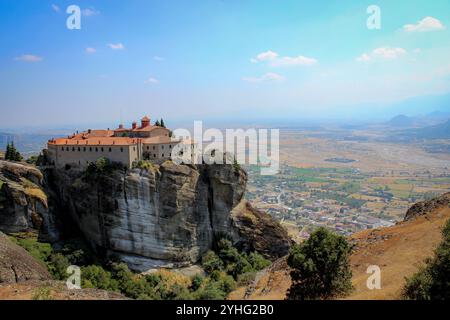 Il Sacro Monastero di Rousanou a Meteora, in Grecia, è arroccato su una roccia torreggiante, con vaste pianure e montagne sullo sfondo. Foto Stock