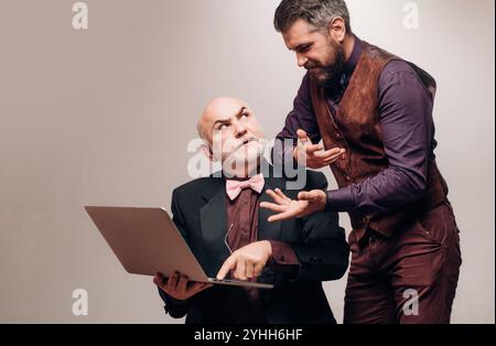 Partner aziendali che utilizzano un notebook. Padre e figlio barbuti ingannano in studio. Un giovane uomo d'affari mostra come usare il computer portatile. Bello Foto Stock