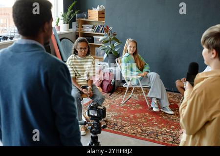 Dietro le quinte di un gruppo di ragazzi adolescenti che registrano podcast o video insieme in studio con l'aiuto dell'insegnante Foto Stock