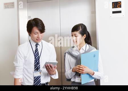 Donna e uomo d'affari che parlano davanti all'ascensore Foto Stock
