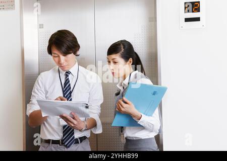 Donna e uomo d'affari che parlano davanti all'ascensore Foto Stock